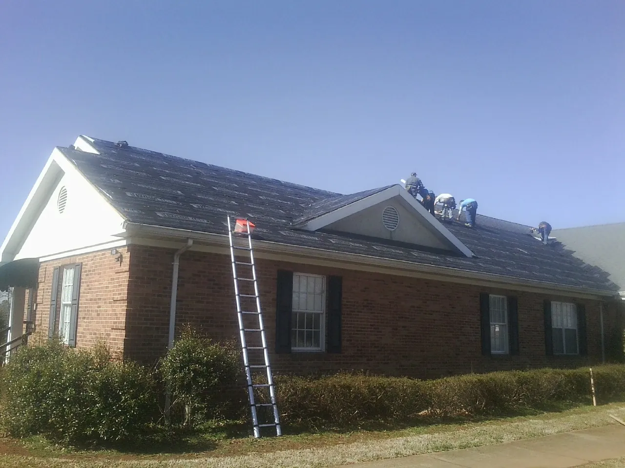 Crew tearing shingles off a brick ranch roof with a ladder set — Emergency Roof Repair work by our crew in Mineral Ridge