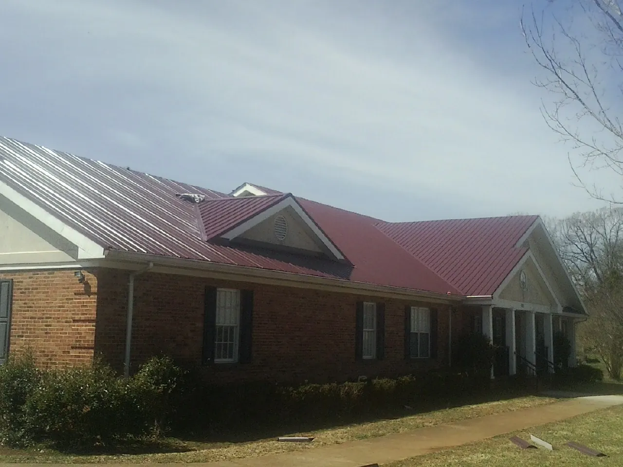 Red metal roof with gabled entries on a long brick building, from a Hail Damage Roof Repair job in Mineral Ridge
