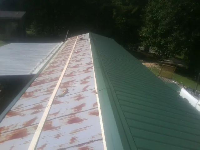 Old rusted panels beside newly installed green metal roofing — Wind Damage Roof Repair by Roofing Brothers in Mineral Ridge