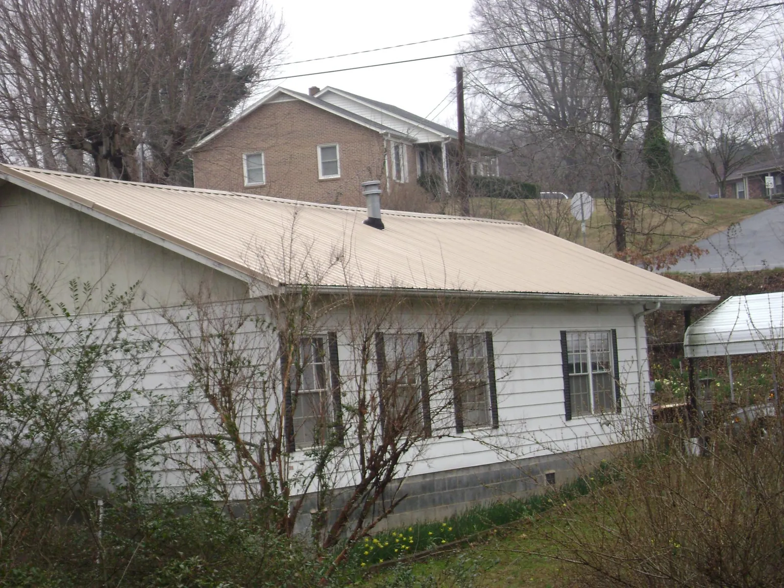 Tan metal roof on a white sided house set into a hillside — Commercial Roofing by Roofing Brothers in Mineral Ridge